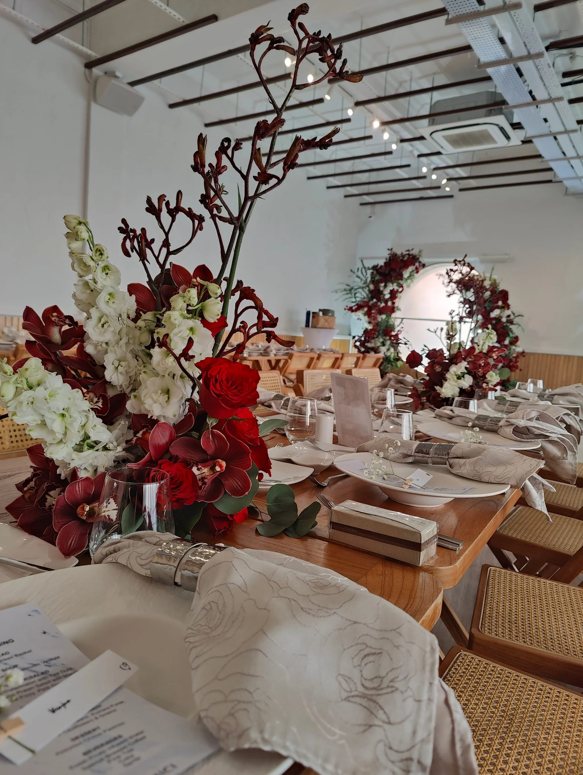 Elegant wedding dinner table at Haus217 with red and white floral centerpieces, linen napkins, glassware, and the venue's circular window visible in the background